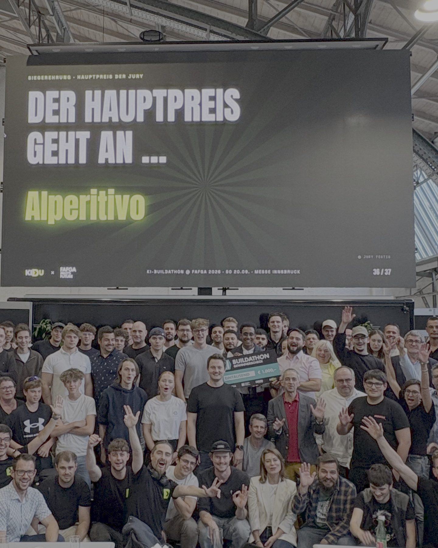 Gruppenbild nach der Siegerehrung: Rund achtzig Teilnehmende stehen und sitzen dicht gedrängt unter der LED-Wand in der Messehalle, viele winken. Auf der Wand steht: Der Hauptpreis geht an Alperitivo.