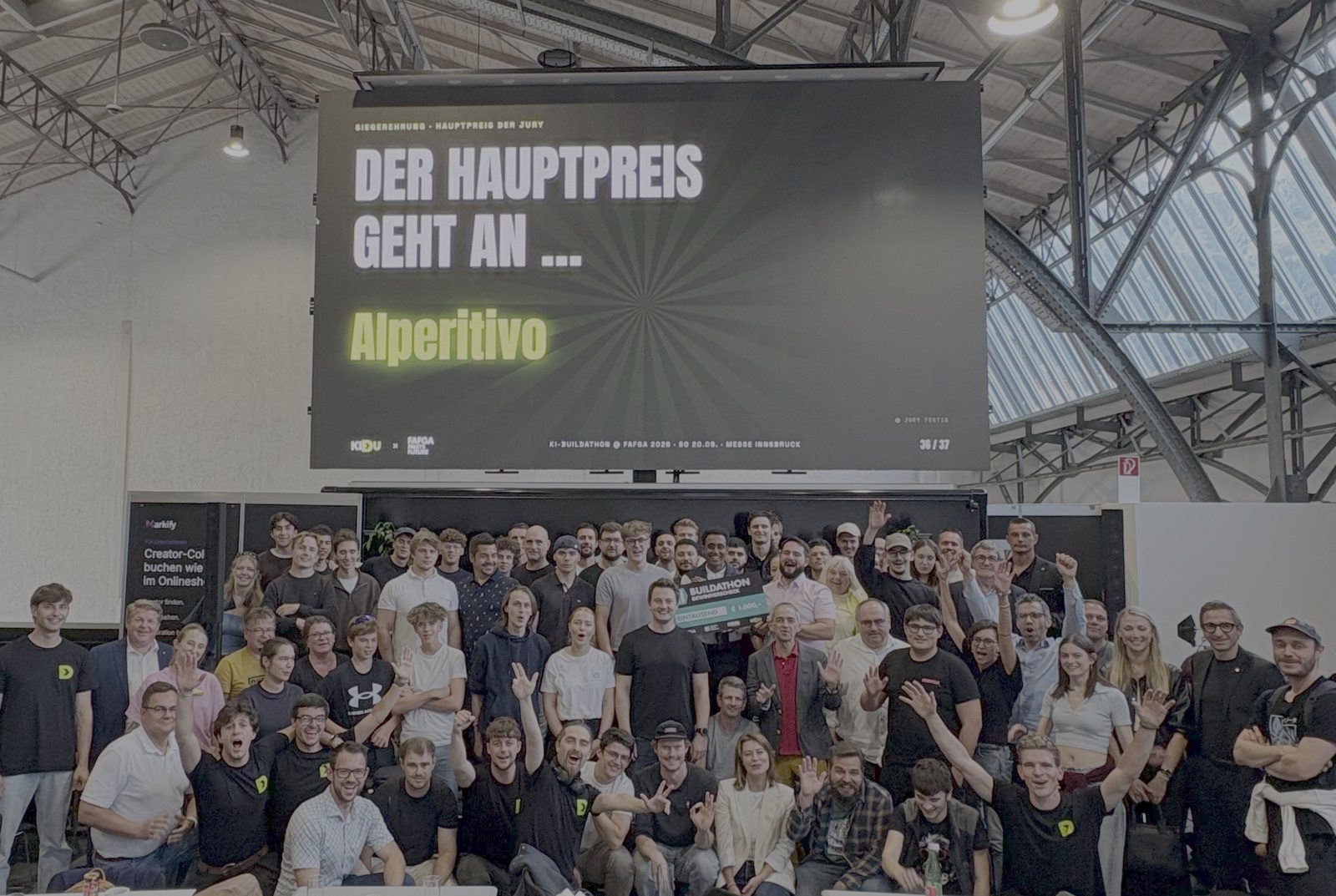 Gruppenbild aller Teilnehmenden nach der Siegerehrung, dicht gedrängt unter der LED-Wand in der Messehalle. Auf der Wand steht: Der Hauptpreis geht an Alperitivo.