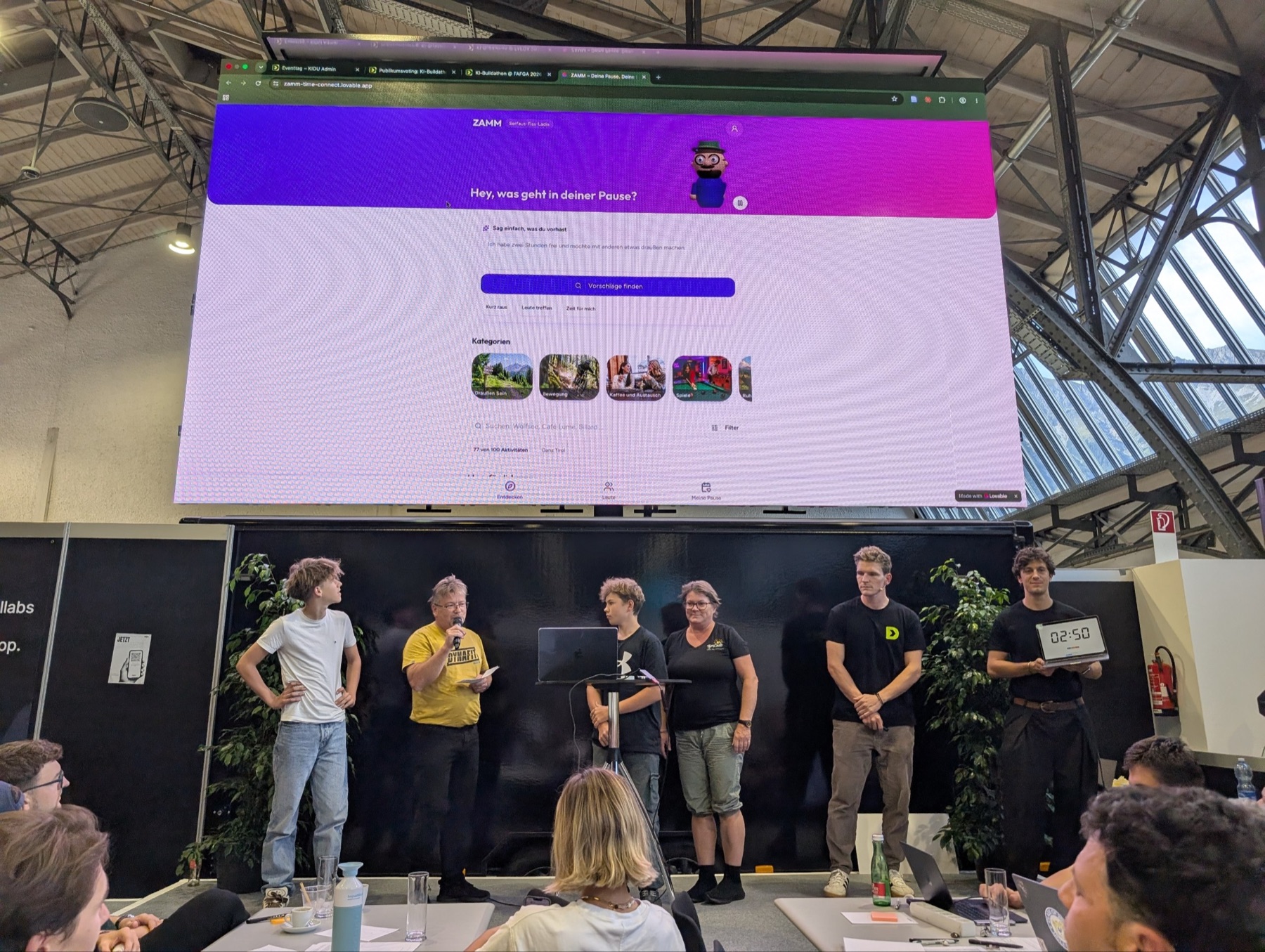 Ein Team steht auf der Bühne, über ihm zeigt die LED-Wand groß den abgegebenen Prototyp.